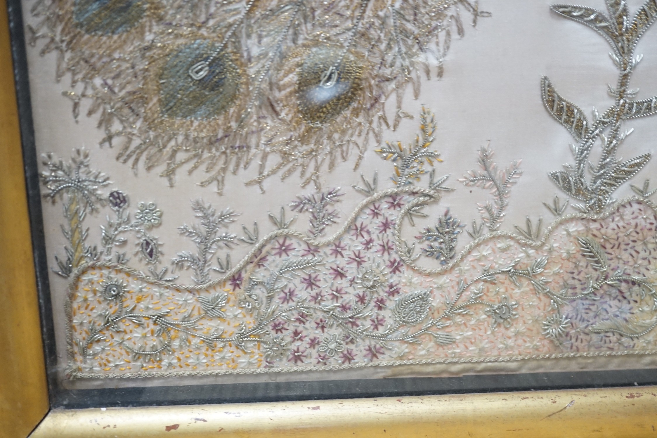 A framed silk, multi coloured metal thread embroidered Indian panel: a peacock seated amongst birds, flowers and leaves in a tree, 110cms x 51cms